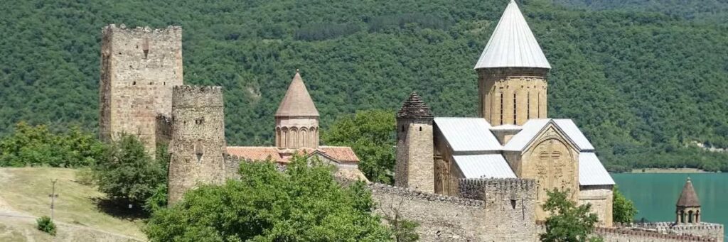 Georgien Reise: Historische Festung Ananuri am Aragwi‑Fluss mit steinernen Türmen und Kirchen, umgeben von grünen Hügeln und Kaukasuslandschaft.