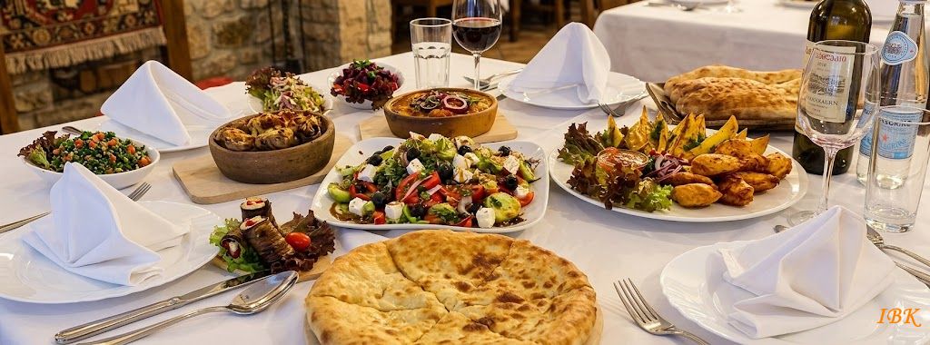 Georgische Tafel mit traditionellen Speisen, Brot, Salaten, Fleischgerichten und Wein in einem rustikalen Restaurantambiente.