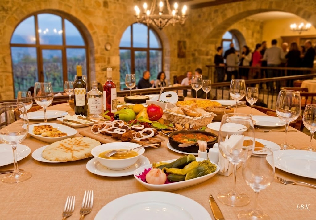 Festlich gedeckte georgische Supra in rustikalem Saal mit traditionellen Speisen, Wein, Brot und Fleischgerichten als Ausdruck georgischer Gastfreundschaft